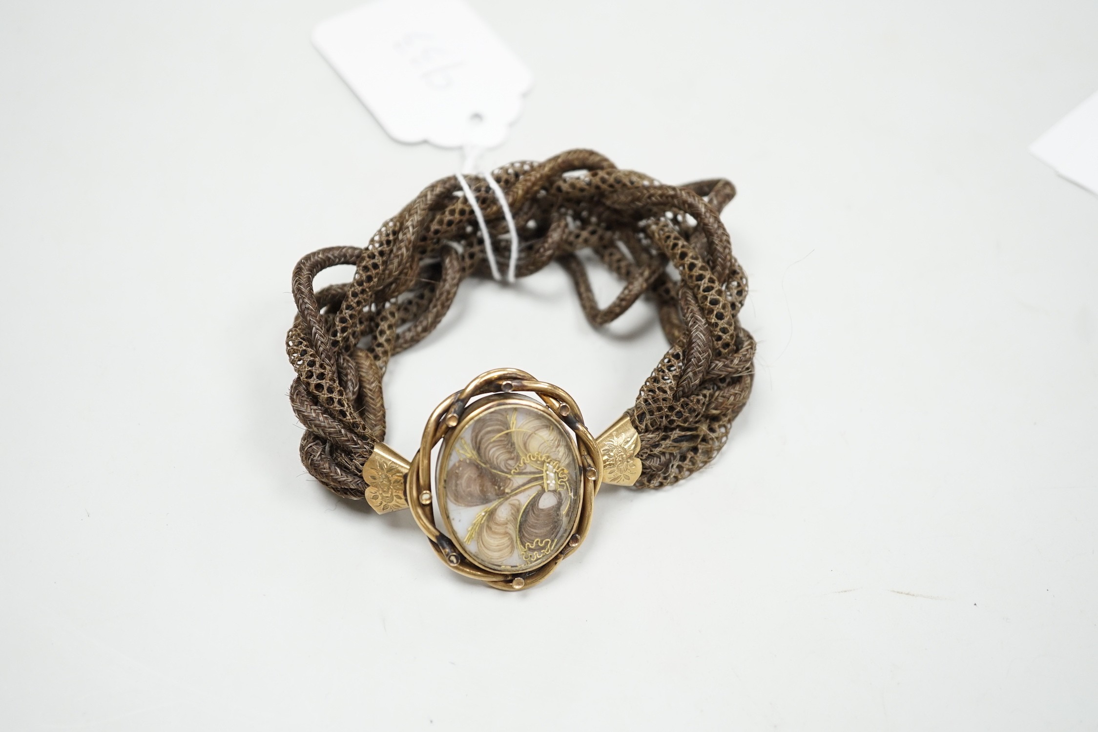 A 19th century gilt metal and plaited hair set interwoven hair mourning bracelet, central motif 41mm by 33mm.